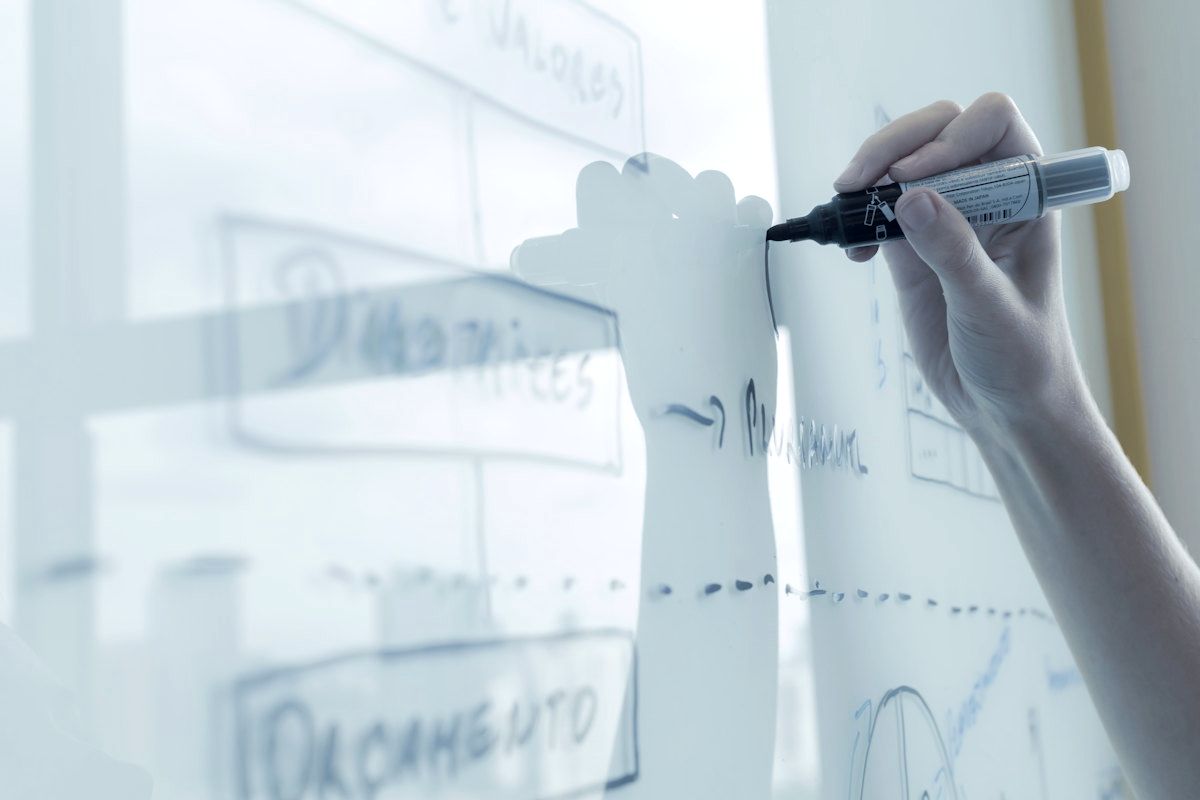 A hand sketching a system diagram on a whiteboard.